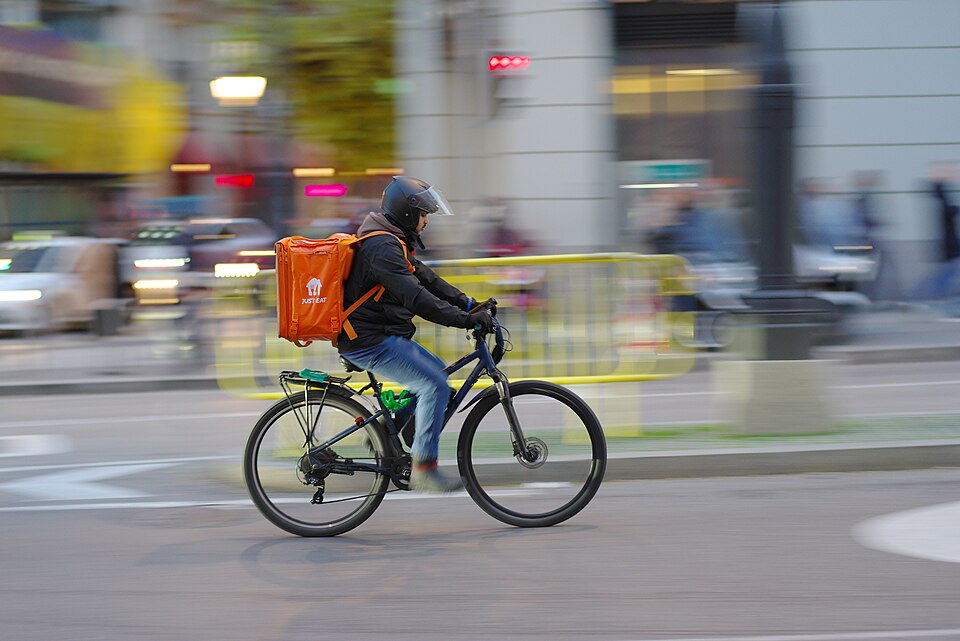 A Just Eat delivery rider in Madrid, shown with his full helmet and bicycle.